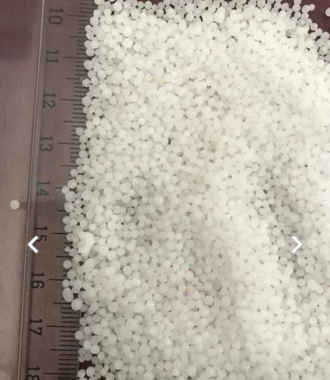 Zbliżenie białych granulek substancji sypkiej, z widoczną podziałką centymetrową na boku, sugerującą pomiar wielkości granulek.