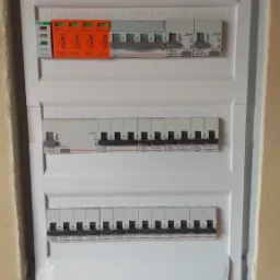 Rozdzielnica elektryczna z zainstalowanymi bezpiecznikami i ochronnikami przepięć Simtec, widoczne oznaczenia i parametry urządzeń, zamontowana w ścianie.