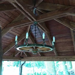 Elcom vision security - Żyrandol w stylu rustykalnym, wykonany z koła od wozu, zawieszony na łańcuchach pod drewnianym zadaszeniem altany.