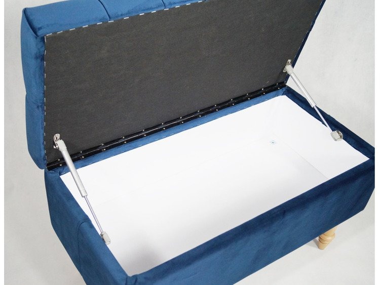 Otwierana, tapicerowana na niebiesko skrzynia z mechanizmem podnoszącym, widoczne drewniane nóżki i białe wnętrze.