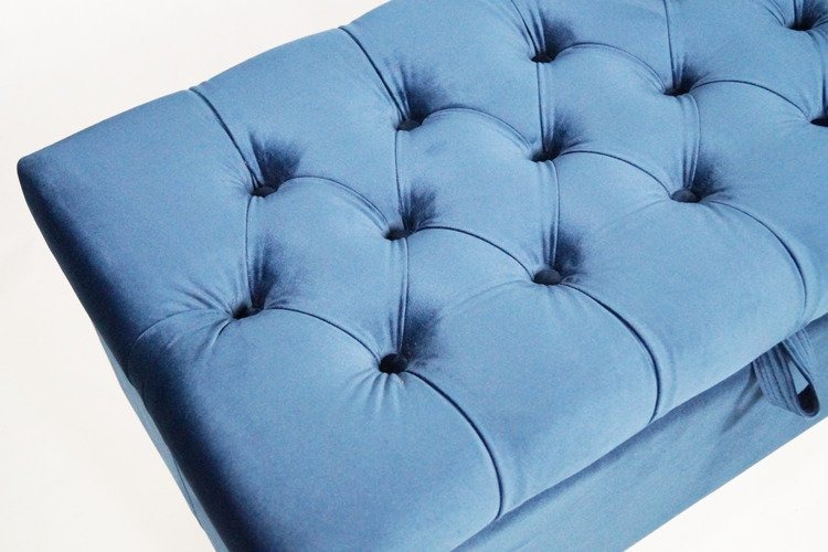 Niebieski puf tapicerowany z głębokimi pikowaniami i guzikami, widok z góry na jasnym tle.