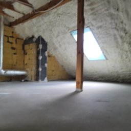Izolator - Poddasze po ociepleniu pianką PUR, widoczne krokwie, okno dachowe i fragment instalacji wentylacyjnej na ścianie, surowy beton na podłodze.