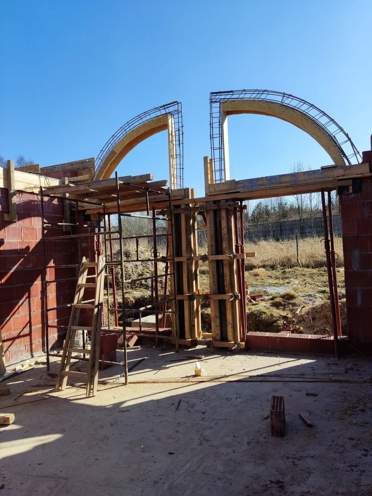 Wznoszenie murów z pustaków ceramicznych z drewnianym szalunkiem łukowym i zbrojeniem, widoczne rusztowanie i drabina