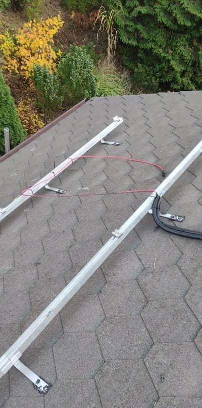 Montaż stelażu pod panele słoneczne na dachu pokrytym gontem bitumicznym; widoczne kable i elementy mocujące.