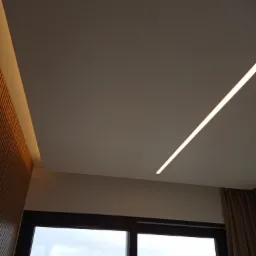 Nowoczesny sufit napinany z oświetleniem LED, widok z okna na budynek mieszkalny.