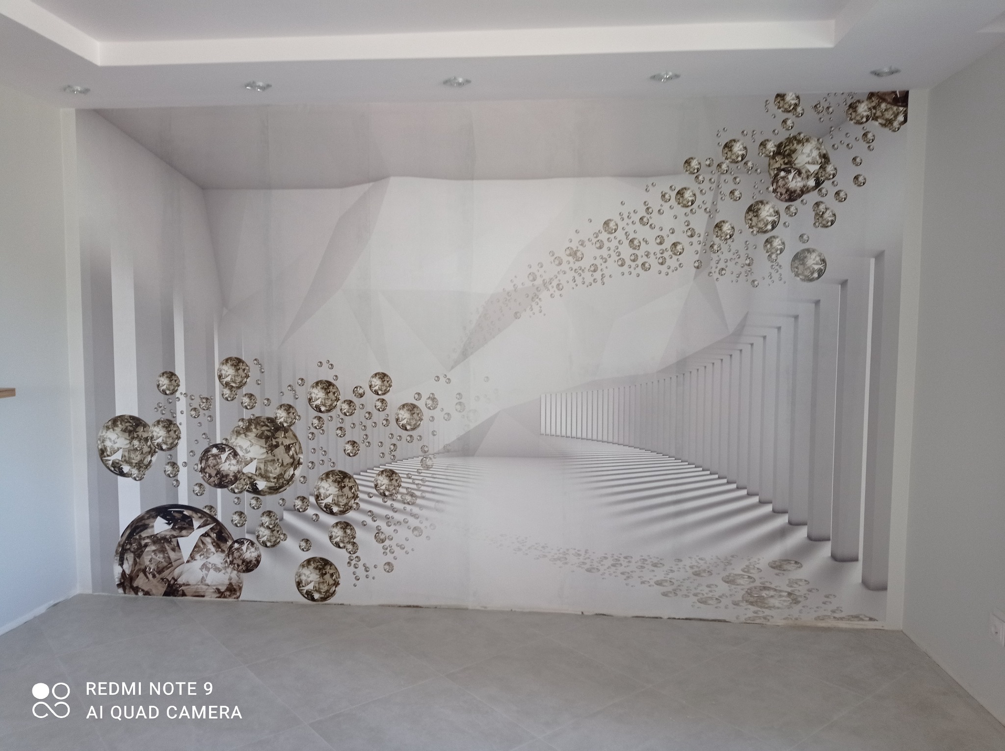 Fototapeta z motywem abstrakcyjnym, przedstawiająca iluzję tunelu z kolumnami i unoszącymi się kulami, umieszczona na ścianie w jasnym pomieszczeniu.