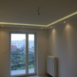 Mich-bud - Nowoczesne wnętrze z oświetleniem LED w suficie podwieszanym, ściana wykończona kamieniem dekoracyjnym, widok na balkon i budynek z okna.