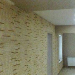 Mich-bud - Korytarz z dekoracyjną ścianą wykończoną panelami imitującymi cegłę, biały grzejnik pod oknem, sufit z oświetleniem punktowym.