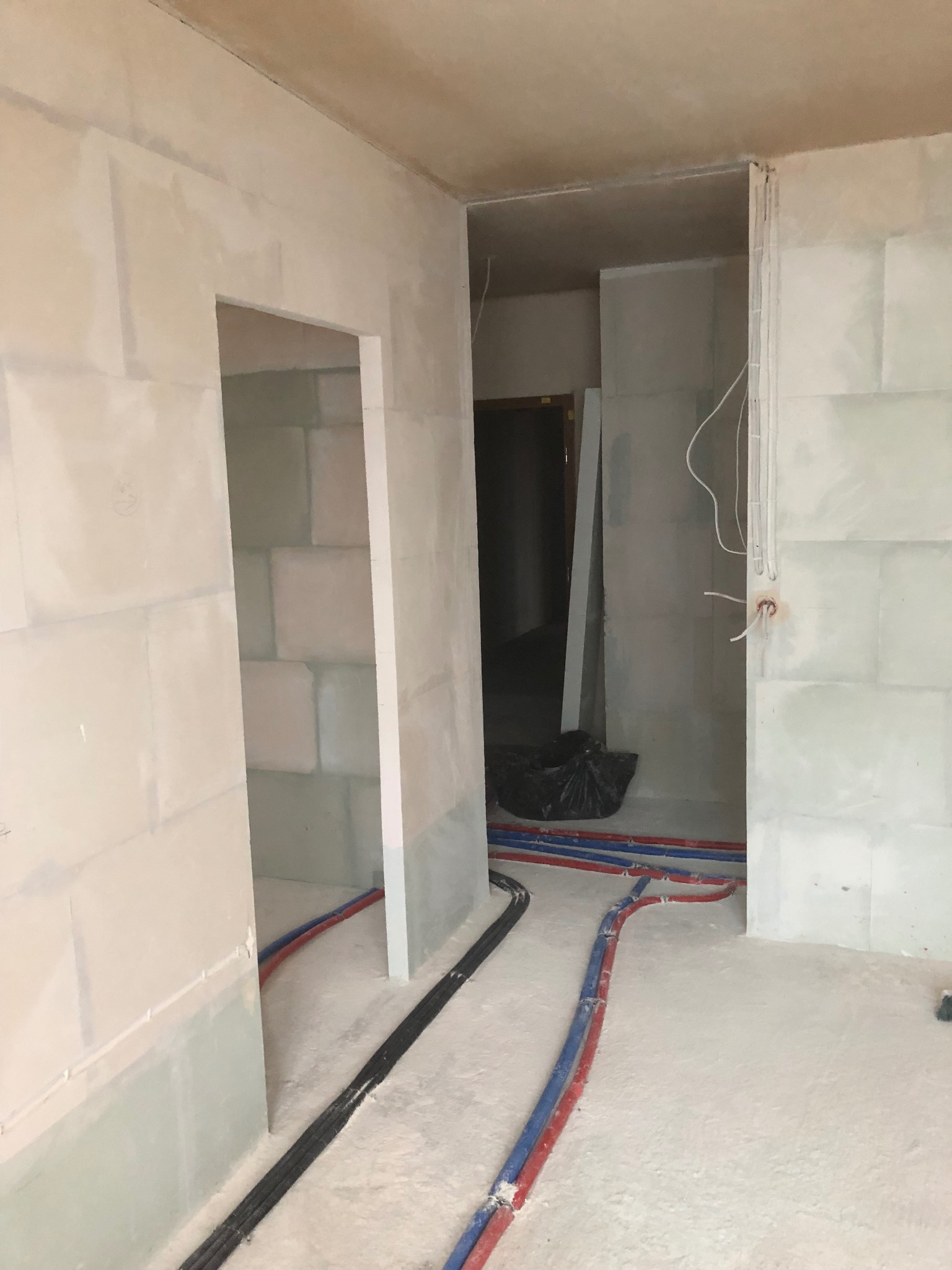 Wnętrze w trakcie prac wykończeniowych: ściany wymurowane z bloczków, wstępnie przygotowane do dalszych prac, widoczne instalacje elektryczne i hydrauliczne na podłodze, ściany z widocznymi śladami...