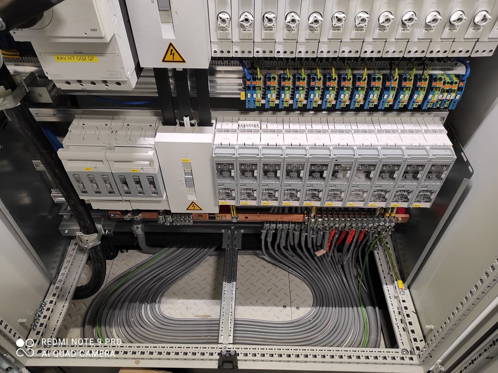 Rozdzielnica elektryczna z zainstalowanymi bezpiecznikami, okablowaniem i oznaczeniami ostrzegawczymi, widok z góry pod lekkim kątem.