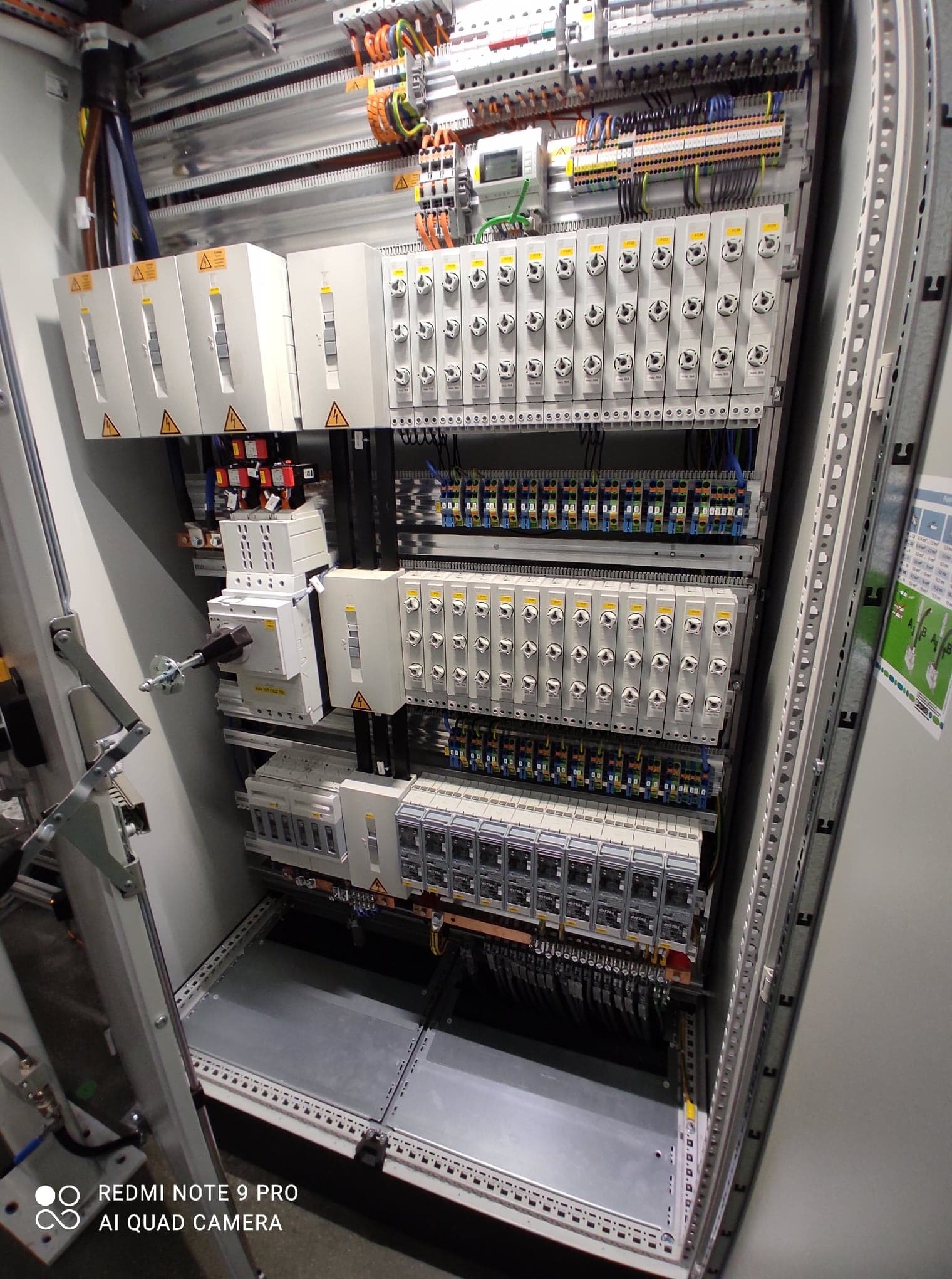 Otwarta szafa sterownicza z widocznymi zabezpieczeniami, okablowaniem i elementami sterującymi, z bliska, oświetlenie górne.