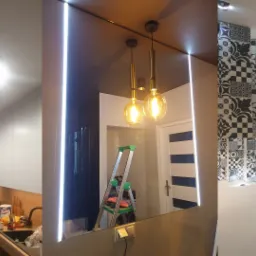 Wnętrze mieszkania po remoncie: nowoczesna kuchnia z niebieskimi szafkami, lustrzana ściana z oświetleniem LED, wiszące lampy i dekoracyjna ściana z czarno-białych płytek.