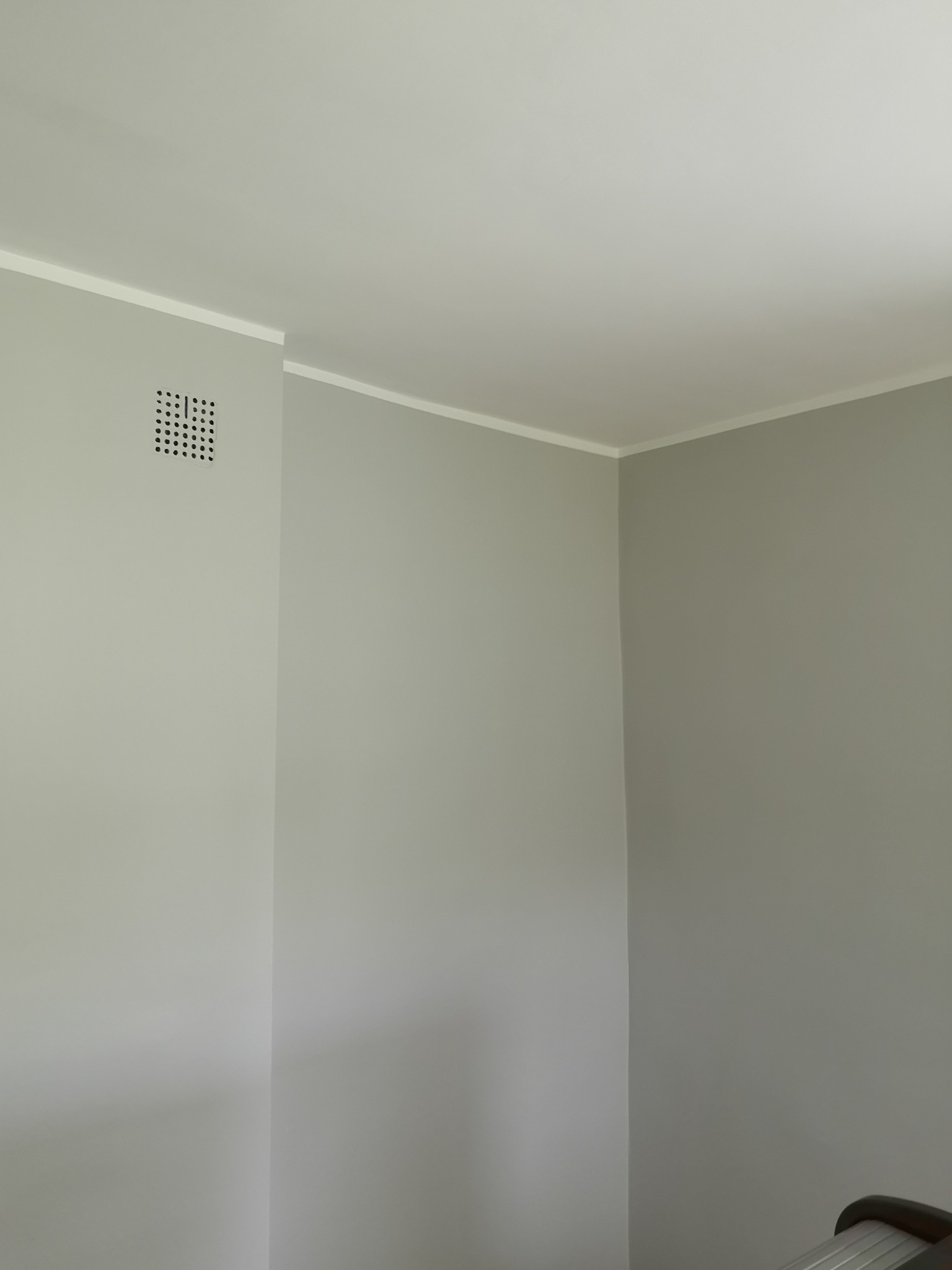 Świeżo pomalowane wnętrze w odcieniach szarości z białą listwą sufitową i kratką wentylacyjną przy suficie na ścianie