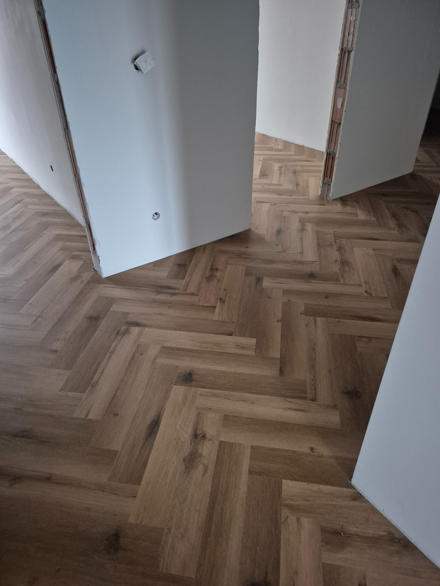 Ułożona podłoga z paneli w jodełkę, widok z góry, jasne panele drewnopodobne, surowy stan ścian, widoczne fragmenty instalacji elektrycznej.