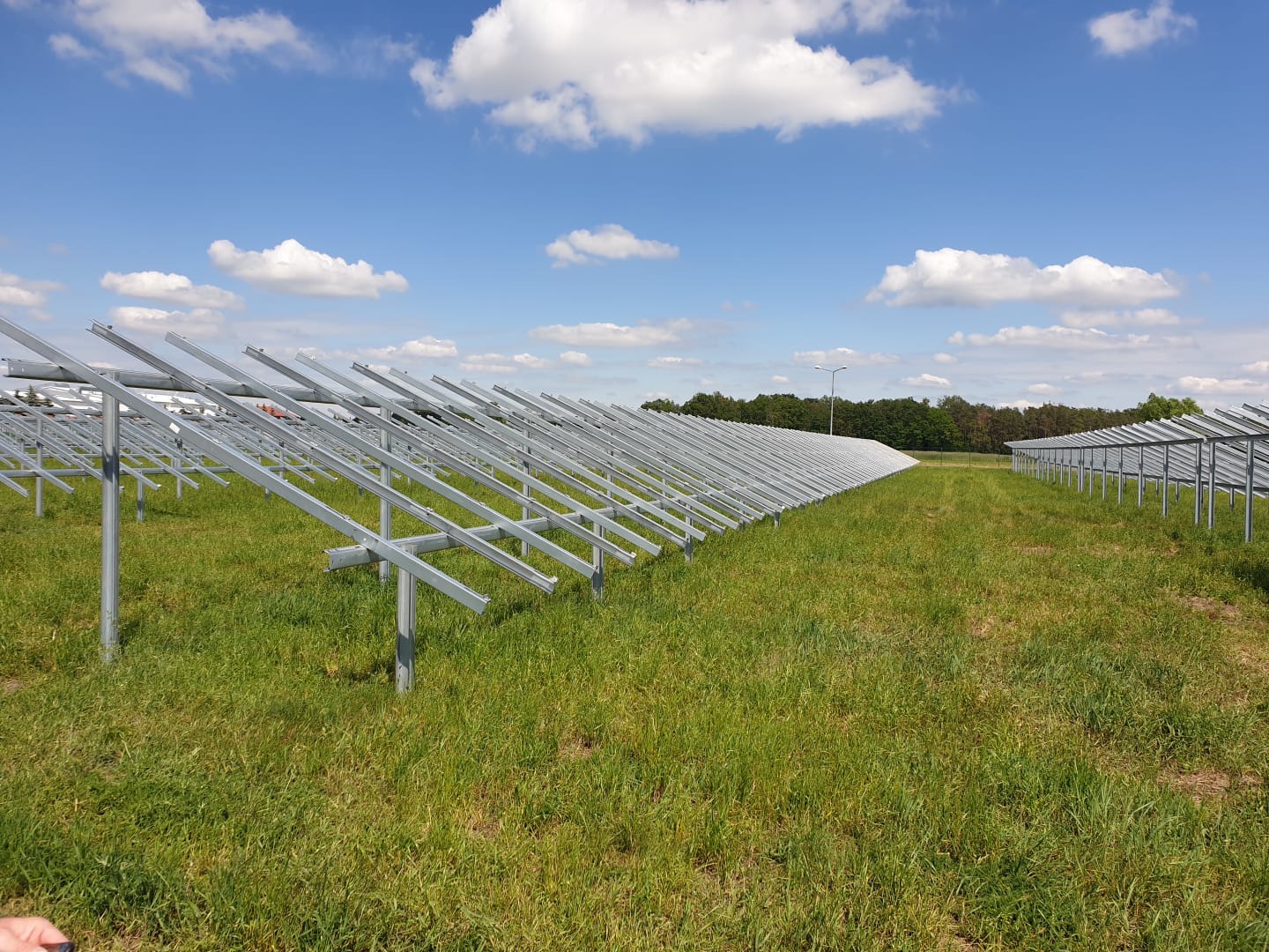 Metalowa konstrukcja wsporcza pod panele słoneczne na trawiastym polu pod błękitnym niebem z chmurami.