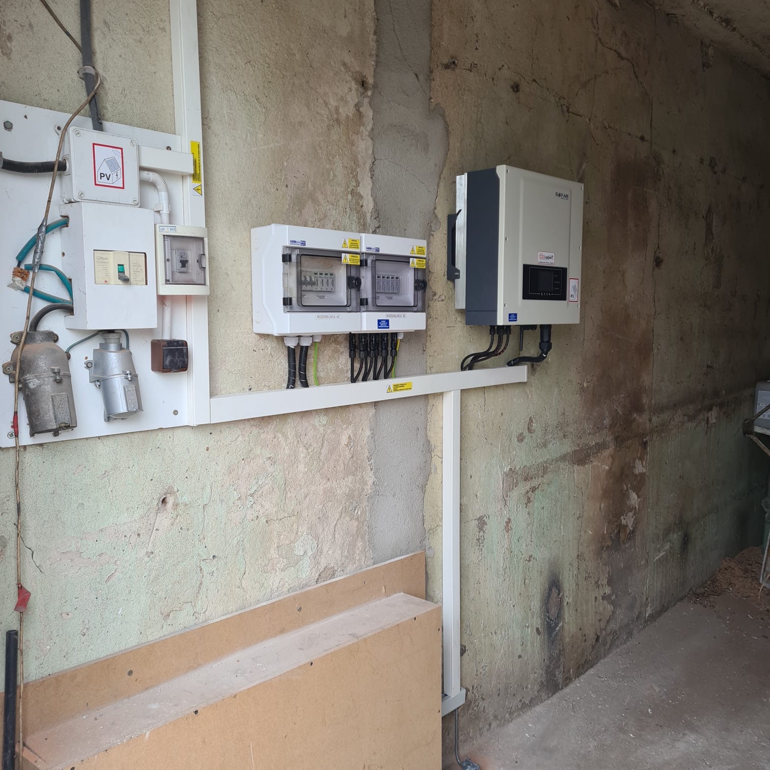 Instalacja elektryczna z rozdzielnicą i inwerterem Sofar Solar zamontowana na nierównej, pomalowanej ścianie wewnątrz budynku.