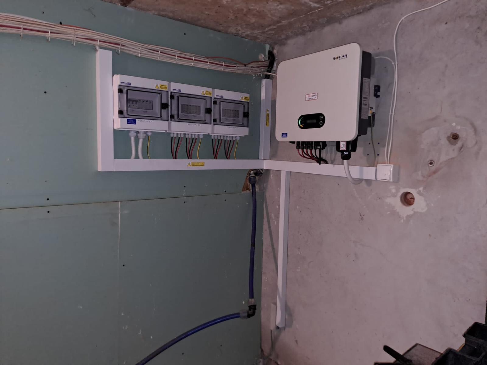 Instalacja inwertera SOFAR i rozdzielni elektrycznej w surowym pomieszczeniu, widoczne kable i rury instalacyjne.