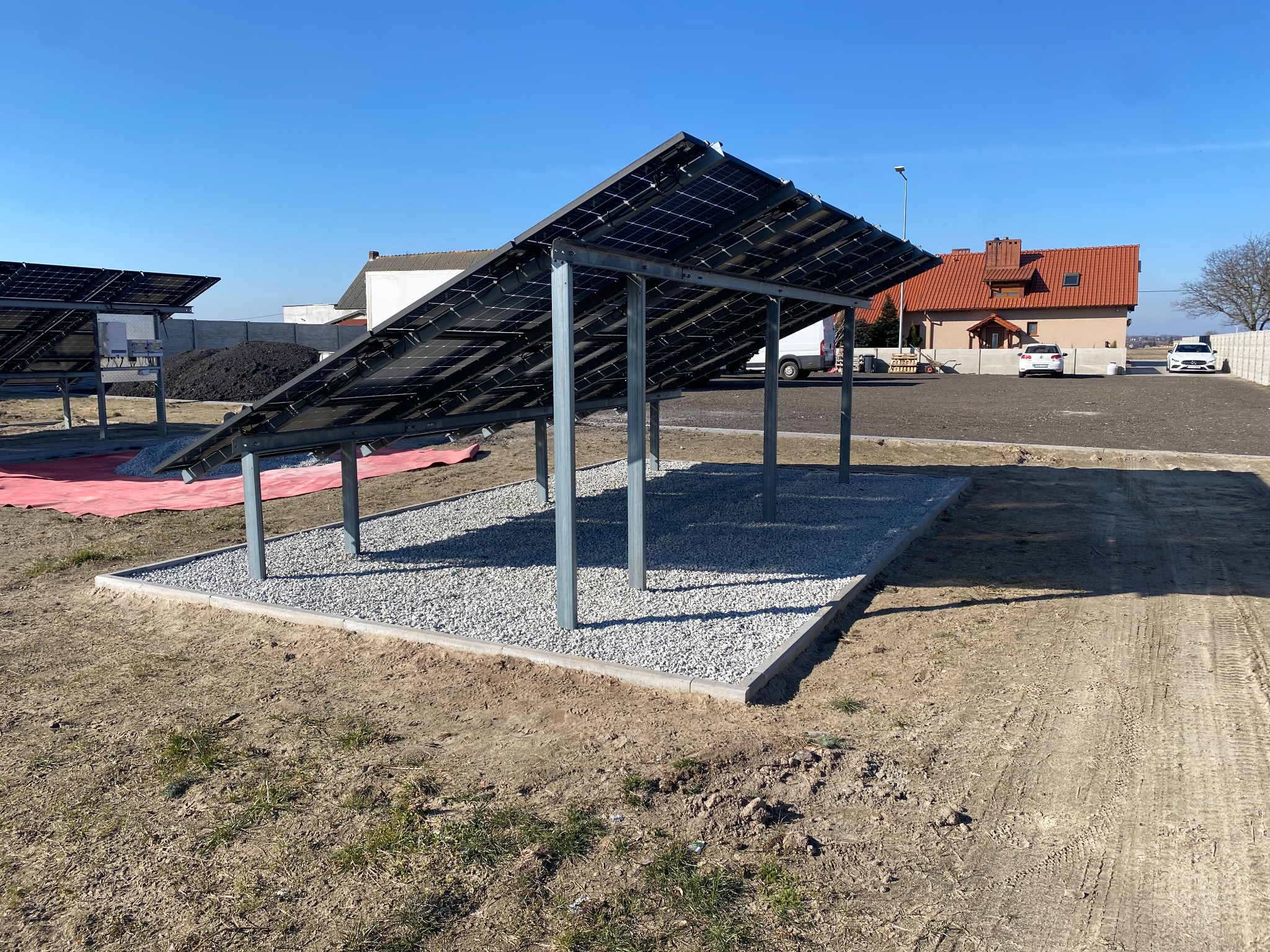 Montaż paneli słonecznych na konstrukcji wsporczej z fundamentem z szarego kamienia na placu budowy w słoneczny dzień.