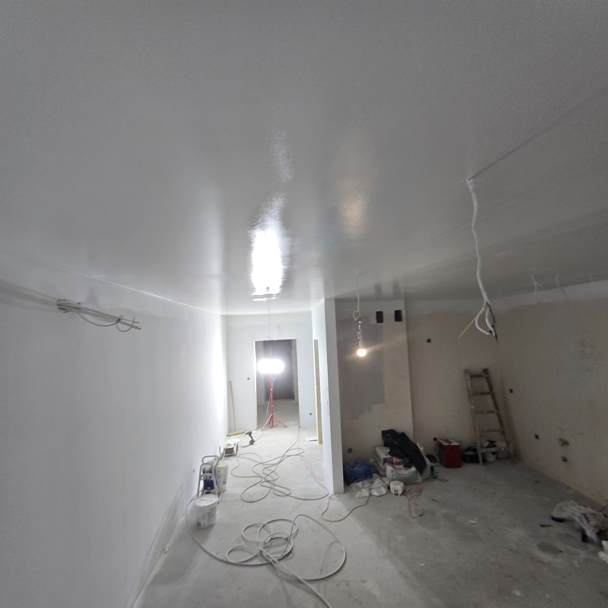 Białe, świeżo pomalowane ściany i sufit w remontowanym wnętrzu, z widocznymi narzędziami malarskimi i drabiną. Nowe, jednolite wykończenie.