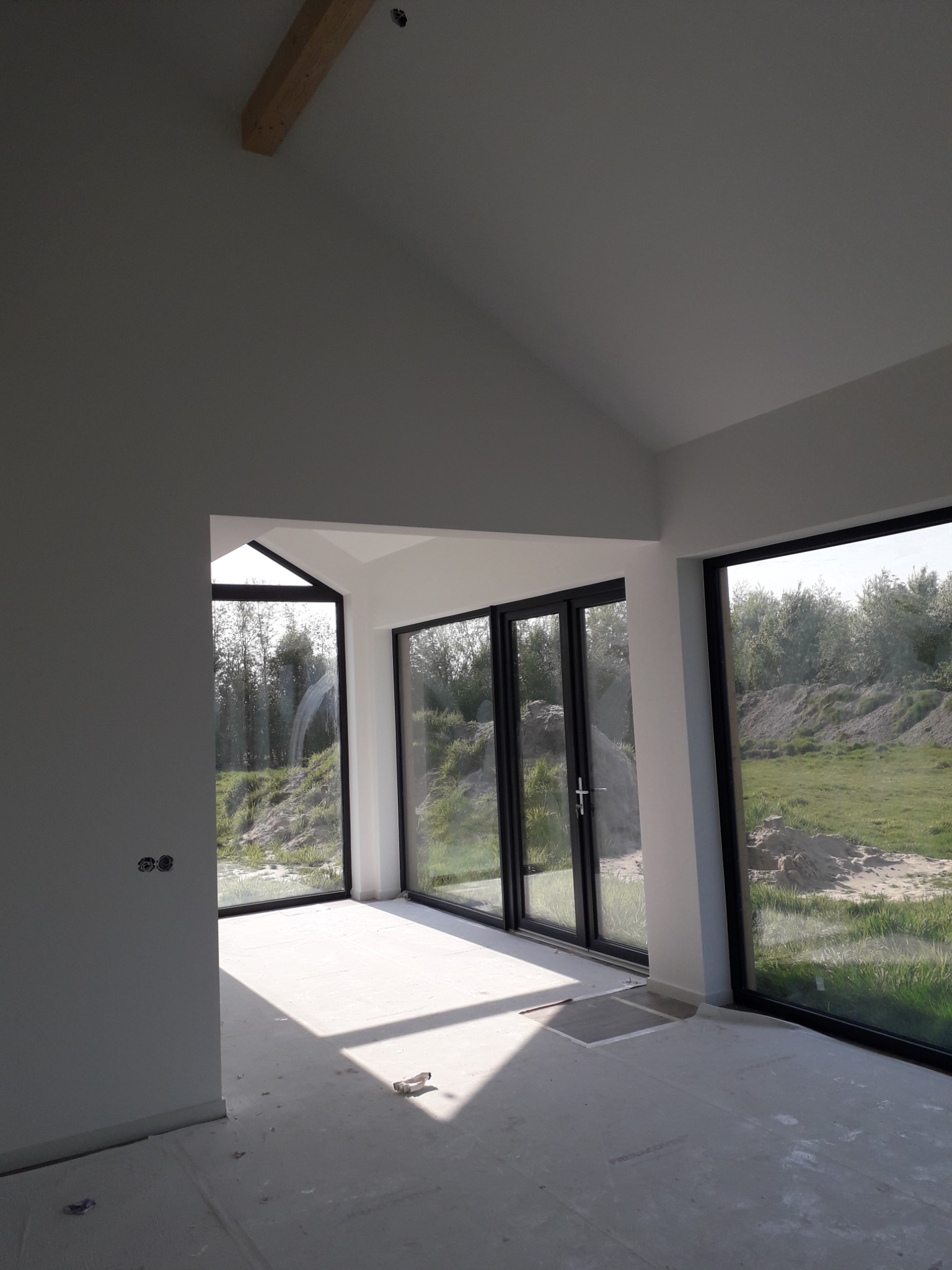 Wnętrze domu w stanie deweloperskim z dużymi oknami i surowymi ścianami, przygotowane do dalszych prac wykończeniowych.