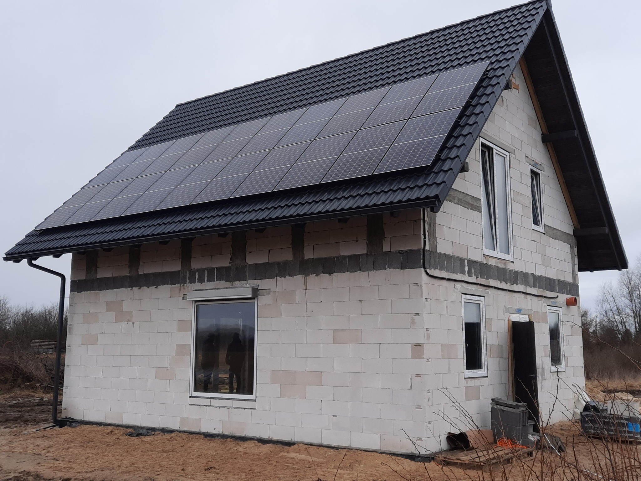 Niedokończony dom z białego pustaka z zamontowanymi panelami słonecznymi na czarnym dachu z blachodachówki.
