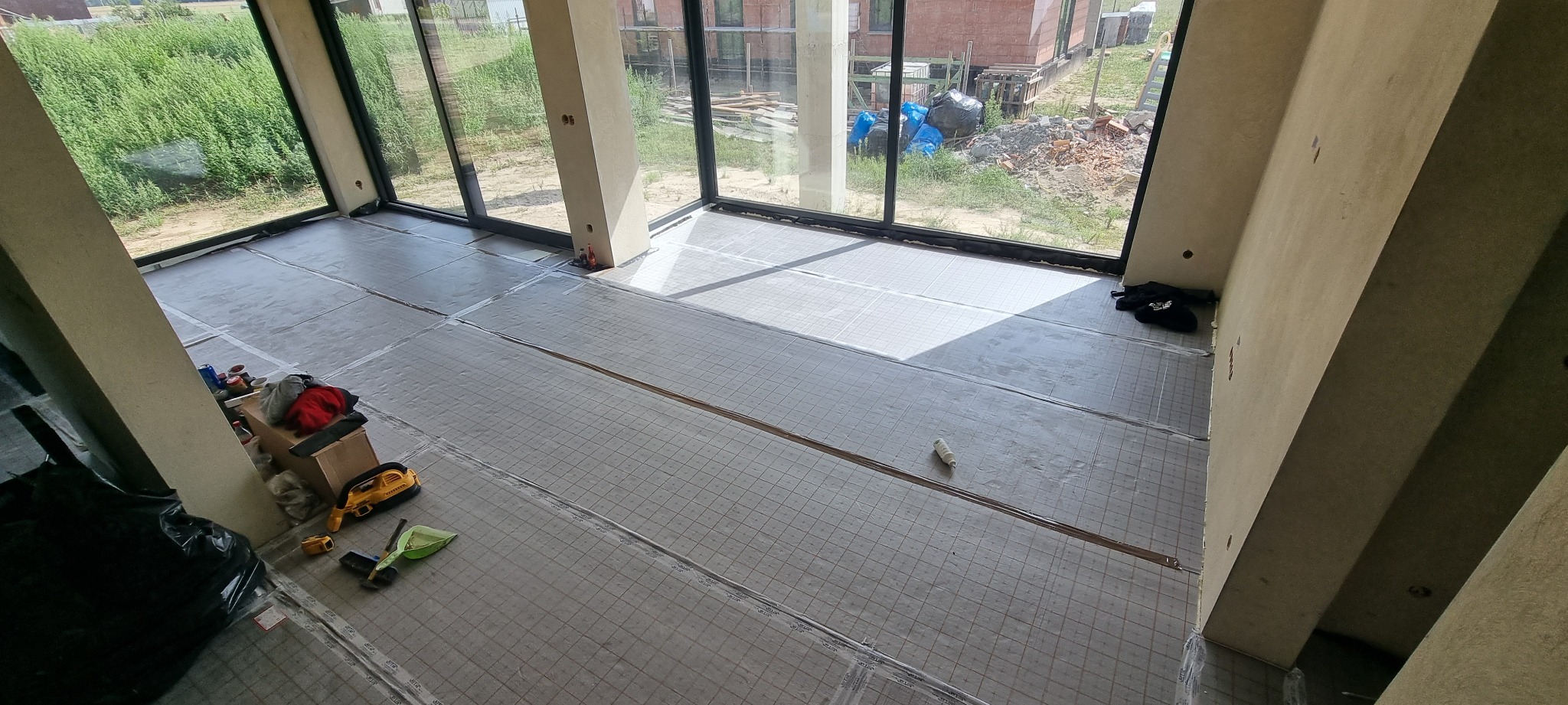 Przygotowanie podłoża pod ogrzewanie podłogowe w nowym budynku, widoczne maty grzewcze z siatką i narzędzia pracy.