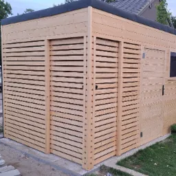 Nowoczesna, drewniana konstrukcja z poziomymi listwami i małym oknem, prawdopodobnie domek narzędziowy, na tle zieleni i samochodu.