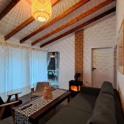 Przytulne wnętrze z drewnianym stropem i kominkiem w Długosiodle. W tle widoczny taras, a całość oświetla dekoracyjna lampa. Ciepła atmosfera.