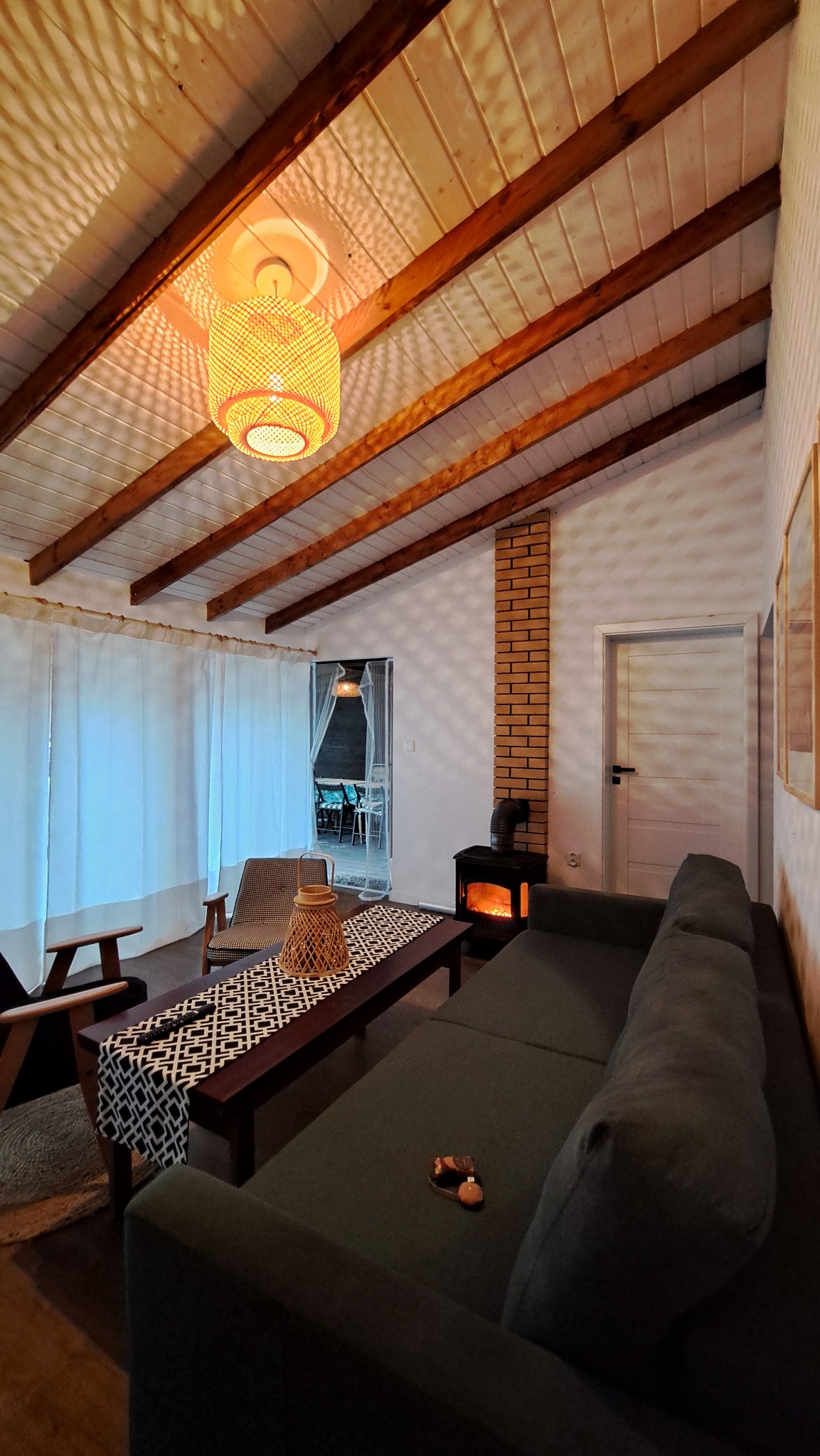 Przytulne wnętrze z drewnianym stropem i kominkiem w Długosiodle. W tle widoczny taras, a całość oświetla dekoracyjna lampa. Ciepła atmosfera.