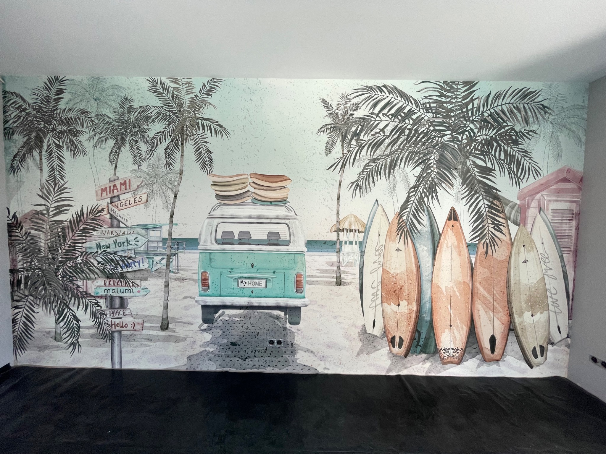 Tapeta przedstawiająca turkusowego Volkswagena Transportera z deskami surfingowymi na dachu, stojącego na tle plaży z palmami, deskami surfingowymi i drogowskazami kierunkowymi do różnych miast.