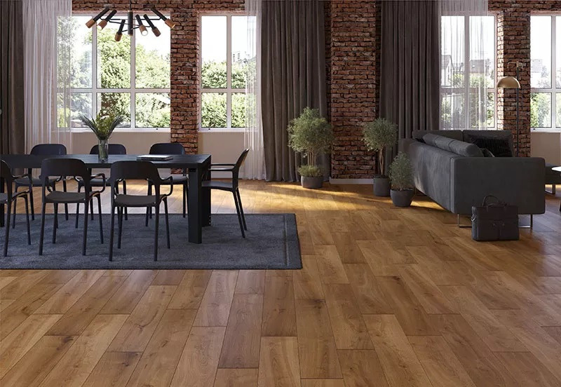 Salon z drewnianą podłogą ułożoną w jodełkę, czarny stół z krzesłami na szarym dywanie, sofa i ceglana ściana w tle.