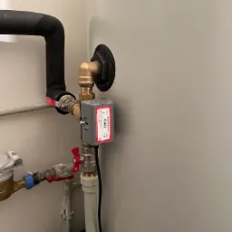 Szczegółowe ujęcie zaworu termostatycznego Honeywell Home UC4013 zamontowanego na rurach instalacji grzewczej, z widocznymi elementami przyłączeniowymi i izolacją termiczną rur.