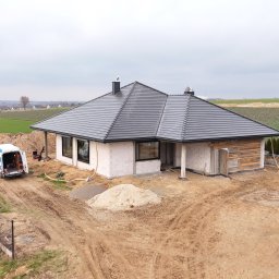 Stolarka otworowa 4K - Dom jednorodzinny w trakcie budowy z czarną dachówką, widoczny z góry, z samochodem dostawczym na posesji i stertami piasku. Budowa w otoczeniu pól.