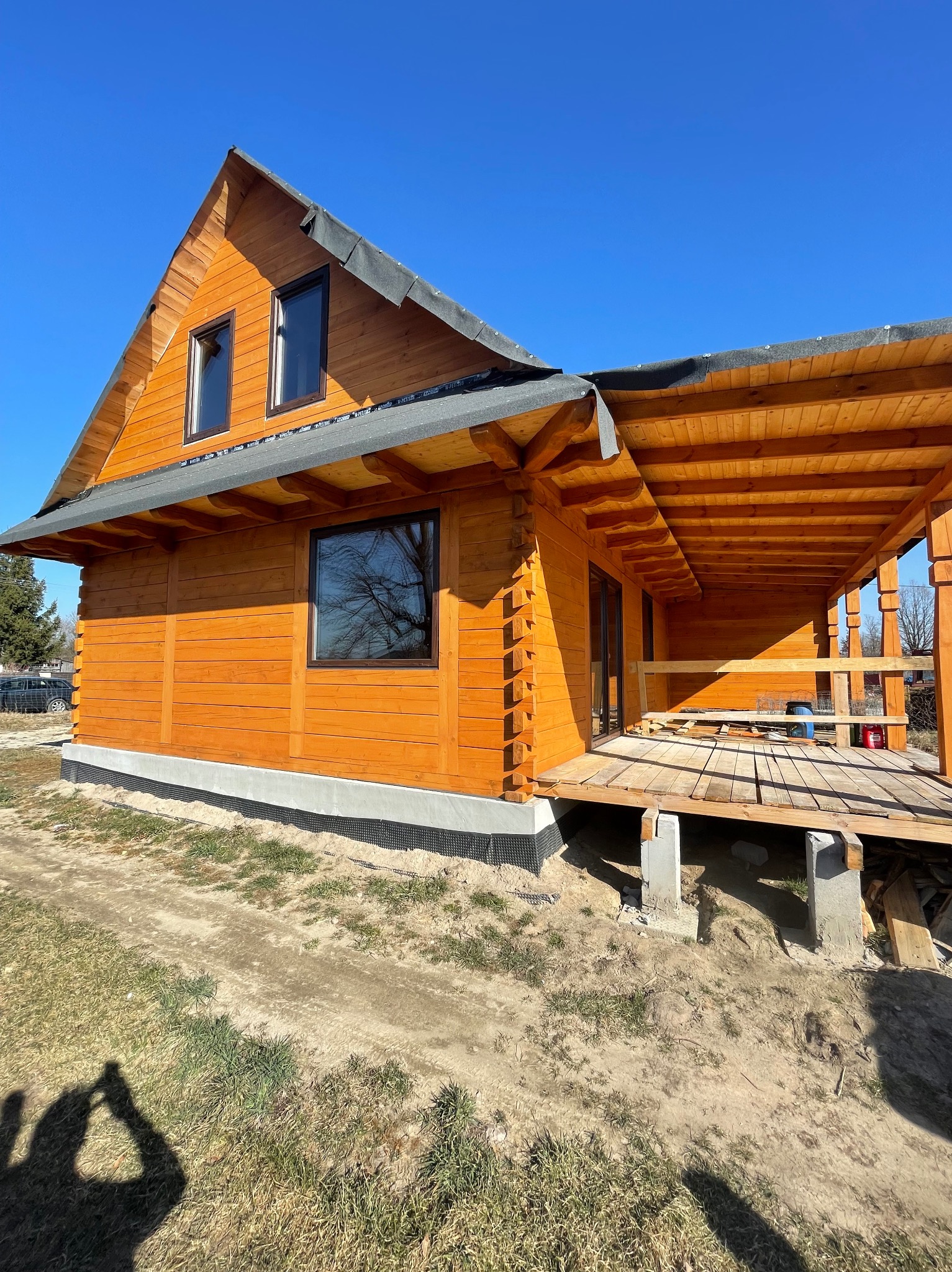 Drewniany dom z oknami w Lublinie, w trakcie budowy, z widoczną konstrukcją tarasu. Elewacja w ciepłym odcieniu brązu, okna z ciemnymi ramami.