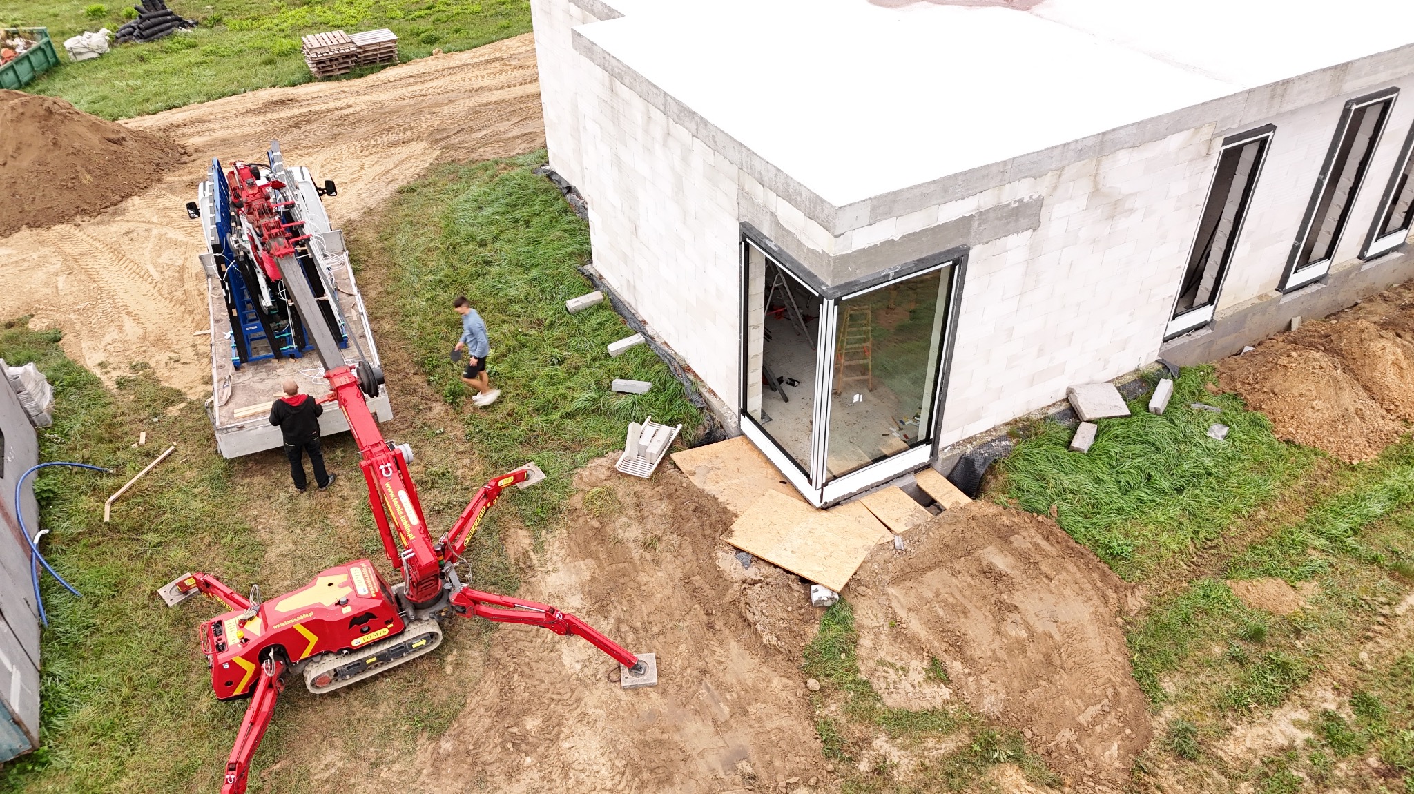 Montaż okna narożnego w surowym budynku z użyciem specjalistycznego dźwigu. Widok z góry ukazuje precyzję i etap prac instalacyjnych.