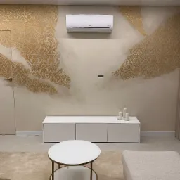 Wnętrze salonu z klimatyzatorem LG Dual Inverter zamontowanym na ścianie z dekoracyjnym, złocistym wzorem, oświetleniem LED pod sufitem, białym stolikiem kawowym i beżowym dywanem.