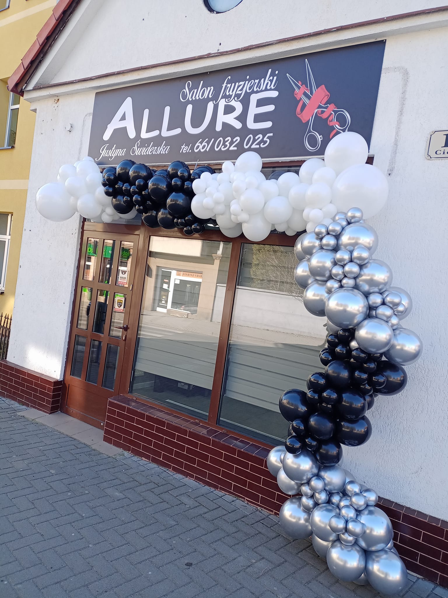 Wejście do salonu fryzjerskiego Allure udekorowane girlandą z czarno-biało-srebrnych balonów.