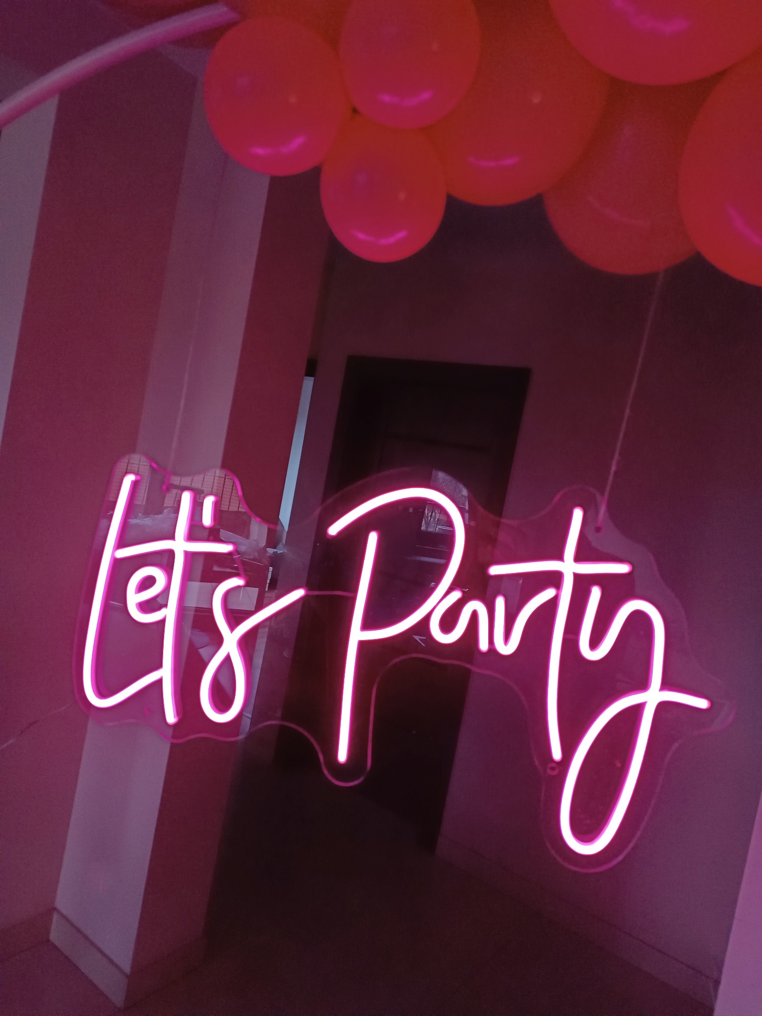 Neonowy napis 'Let's Party' w odcieniach różu, zawieszony pod balonami, tworzący imprezowy nastrój.