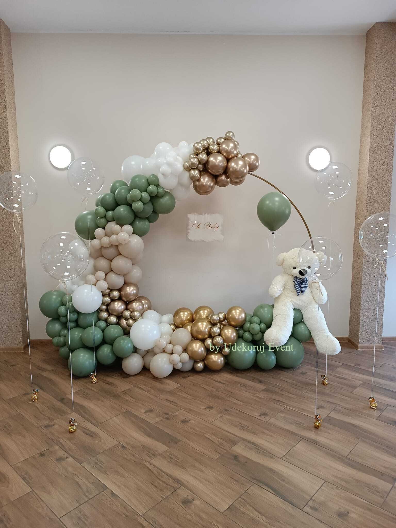 Dekoracja balonowa w kształcie półkola z pluszowym misiem, w kolorach zieleni, bieli i złota, na drewnianej podłodze, z napisem 'Oh Baby'.