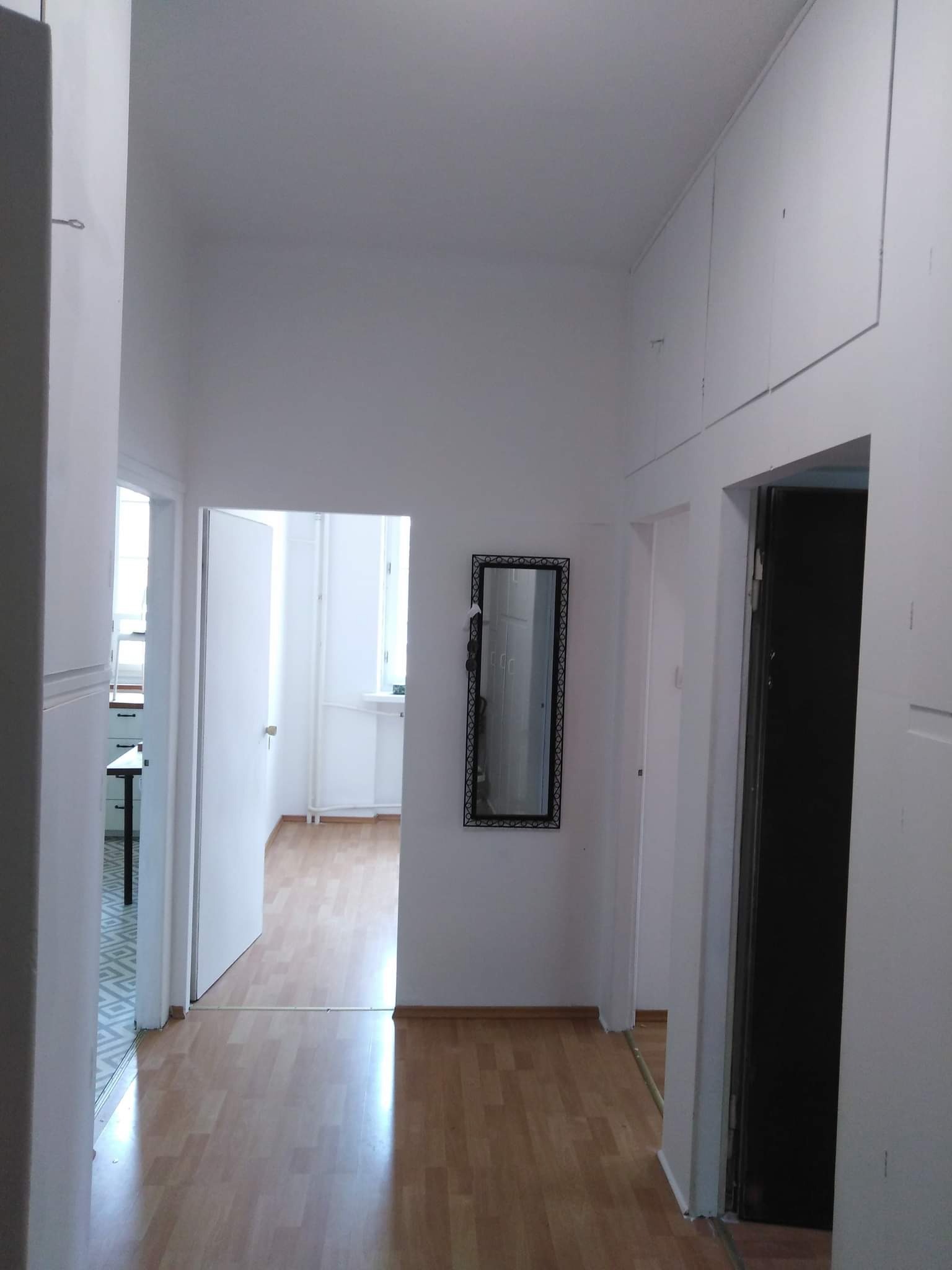 Korytarz po malowaniu na biało, widoczne drzwi, lustro w ozdobnej ramie i zabudowane szafki pod sufitem.