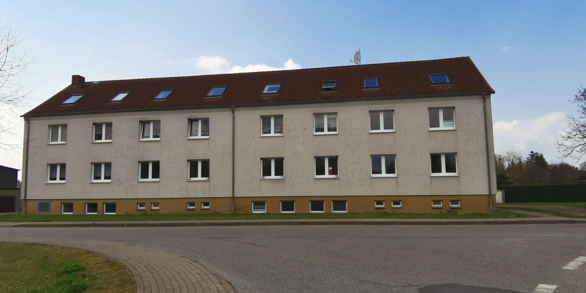 Wielorodzinny budynek mieszkalny w Hamburgu z beżową elewacją, brązowym dachem z oknami połaciowymi i białymi ramami okiennymi, widoczny z poziomu ulicy.