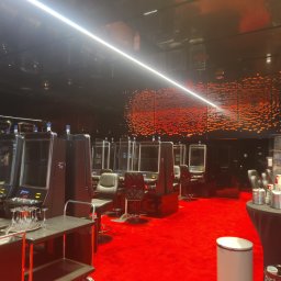 HBK BUDOWNICTWO s.c. - Wnętrze kasyna z rzędem automatów do gier oddzielonych pleksiglasem, czerwona wykładzina, czarne ściany z dekoracją imitującą płomienie, stolik z szklankami i wózkiem barowym.