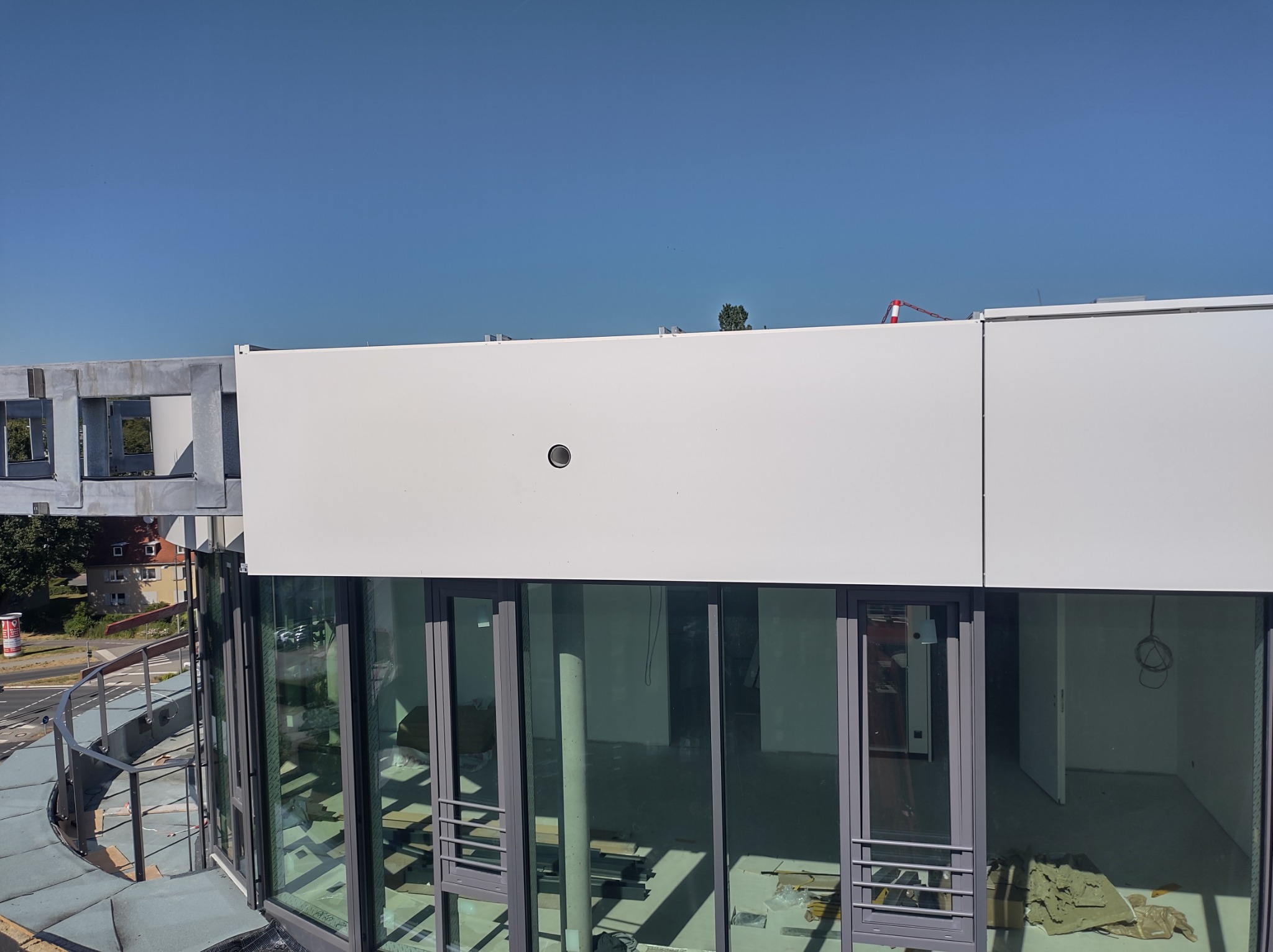 Nowoczesny budynek z białą elewacją i dużymi oknami, widok z góry na balkon z metalową barierką i częściowo wykończone wnętrze.