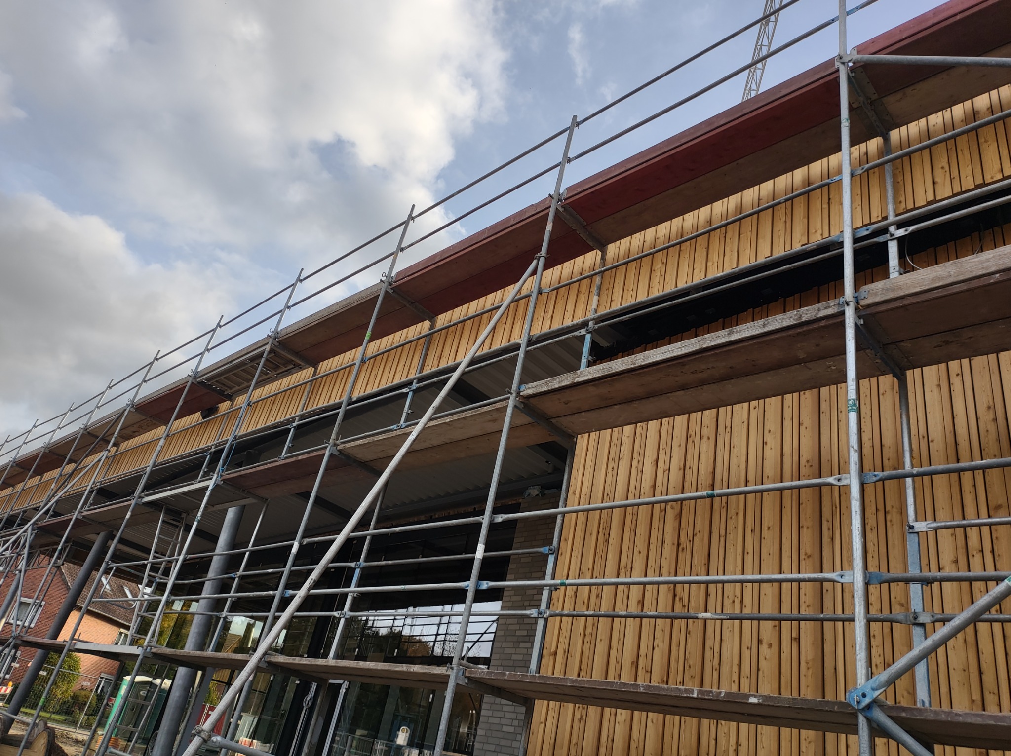 Budynek w trakcie montażu drewnianej elewacji, widoczne rusztowania i fragmenty konstrukcji dachu.