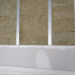 Ocieplenie ściany wełną mineralną, widoczne metalowe profile i częściowo położona gładź gipsowa.