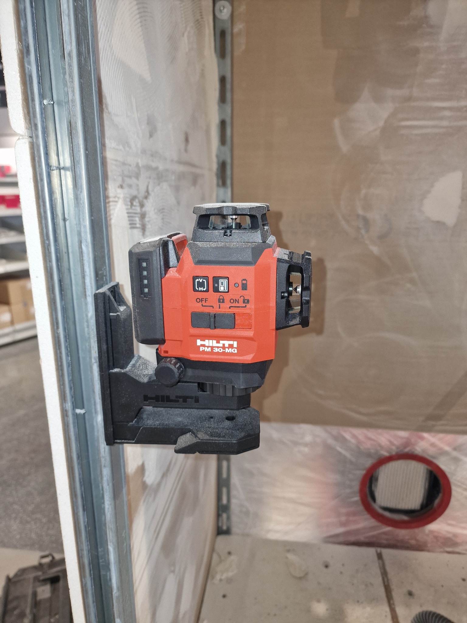 Czerwony laser krzyżowy Hilti PM 30-MG zamocowany na metalowym profilu, widoczny w trakcie pracy na tle ściany przygotowanej do wykończenia.