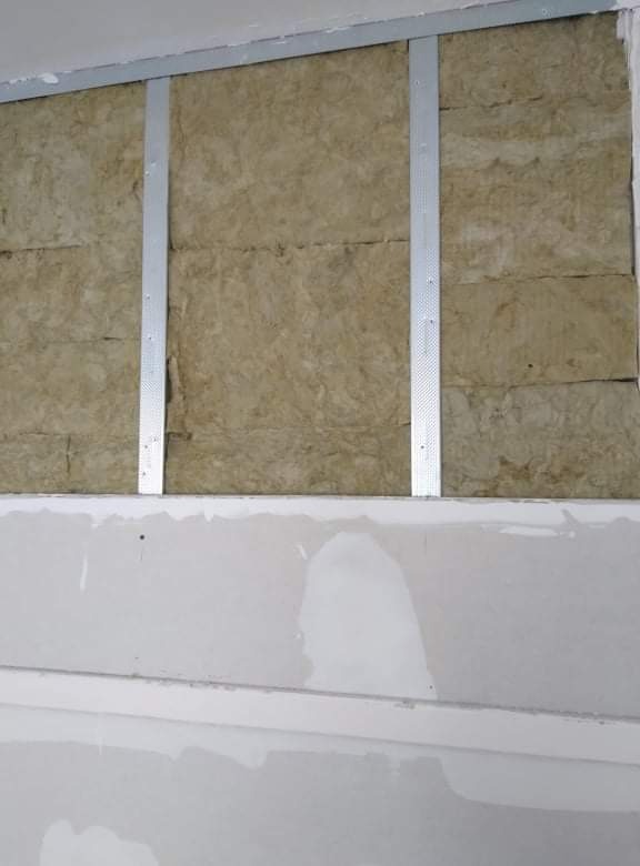 Ocieplenie ściany wełną mineralną, widoczne metalowe profile i częściowo położona gładź gipsowa.