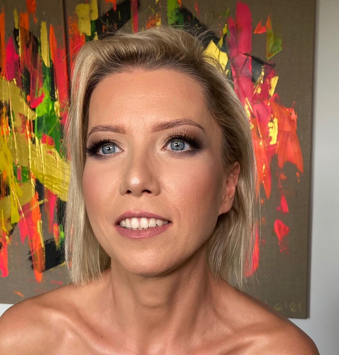 Portret kobiety z blond włosami i profesjonalnym makijażem oczu w odcieniach szarości, na tle abstrakcyjnego obrazu.