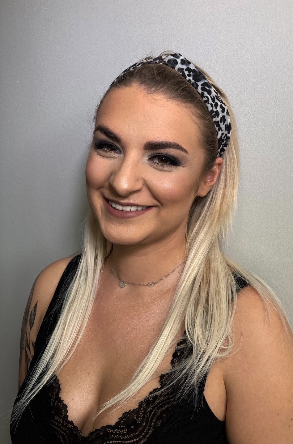 Uśmiechnięta blondynka z intensywnym smoky eye, ozdobną opaską we wzór panterki i delikatną biżuterią, prezentująca efektowny wygląd.