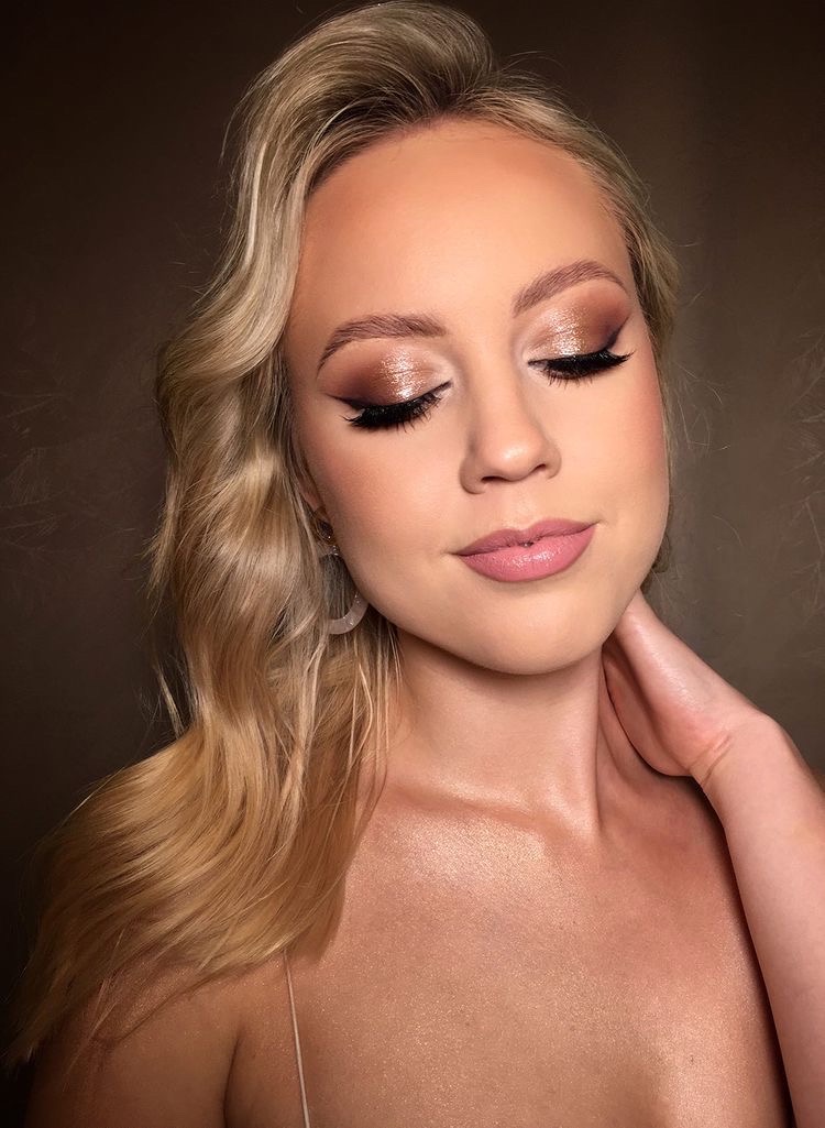 Portret kobiety z zamkniętymi oczami, prezentującej wieczorowy, błyszczący makijaż oczu w odcieniach brązu i beżu z wyraźną kreską, delikatny róż na ustach, blond włosy ułożone w fale i subtelne...